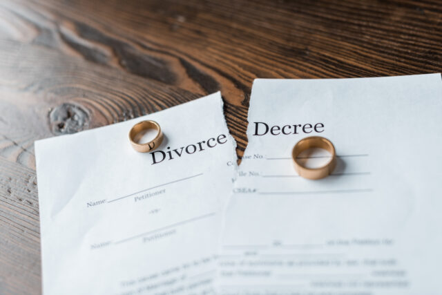 close-up shot of teared divorce decree and engagement rings on wooden surface